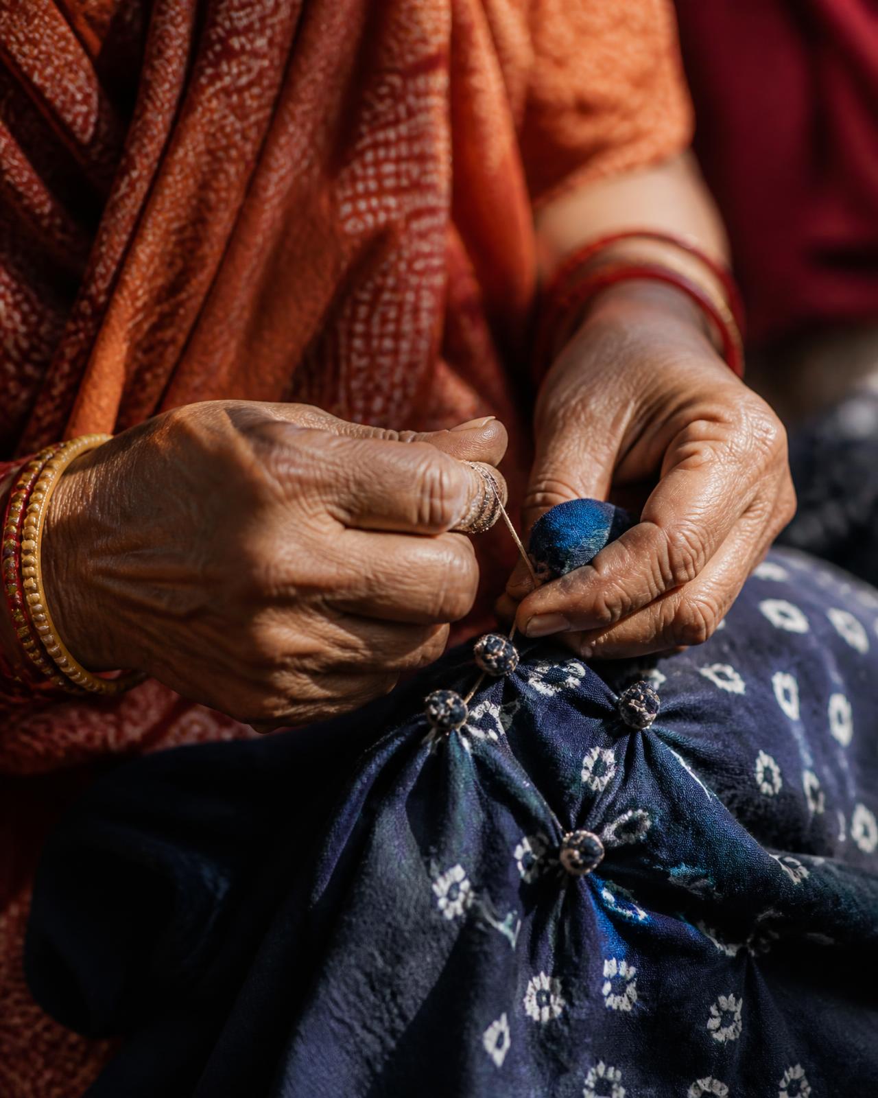 Artisan hands tying Bandhani knots into indigo cotton in Kutch
